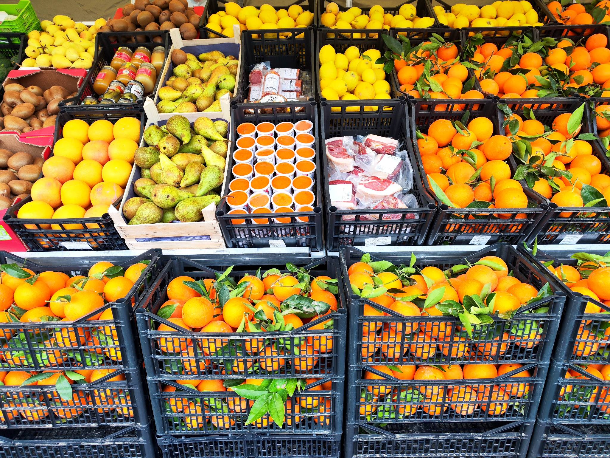 A market stall filled with crates of oranges, lemons, pears, and other fruits.